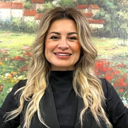 Professional woman with long blonde hair smiling at camera in front of floral garden backdrop