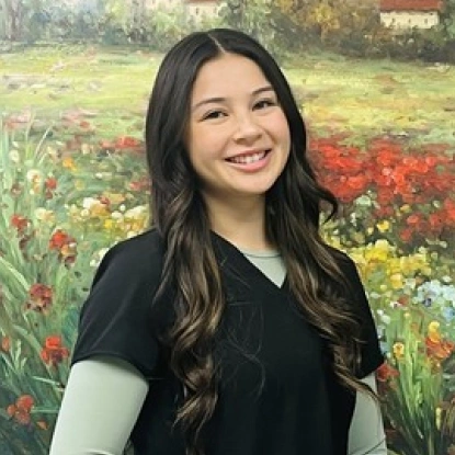 Young woman smiling at camera with colorful flower garden background.