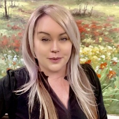 Woman with pink-blonde hair smiling at camera in front of flowering field background.