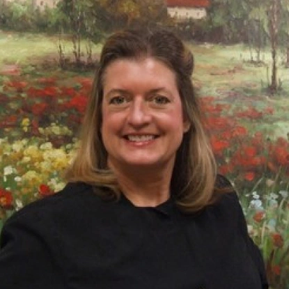 Woman smiling at camera wearing black shirt against colorful flower field background.