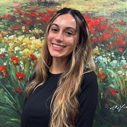 Smiling female dental team member in front of colorful flower garden backdrop.